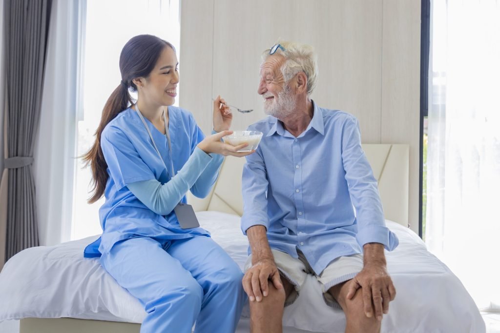 A care worker helping an older man eat a meal at a residential care centre.